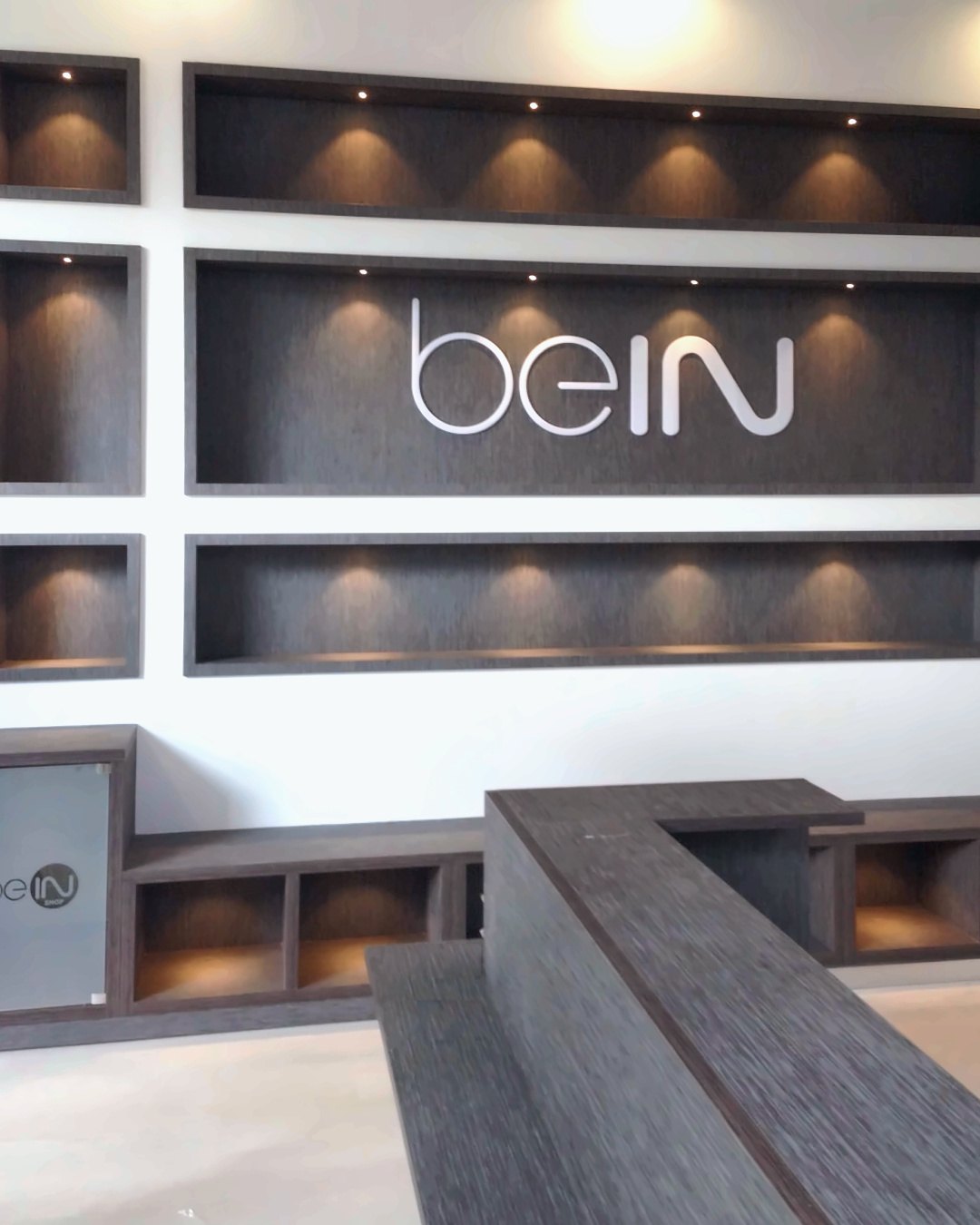 Logovæg med beIN logo og belyste nicher bag skranken i butikken i Doha