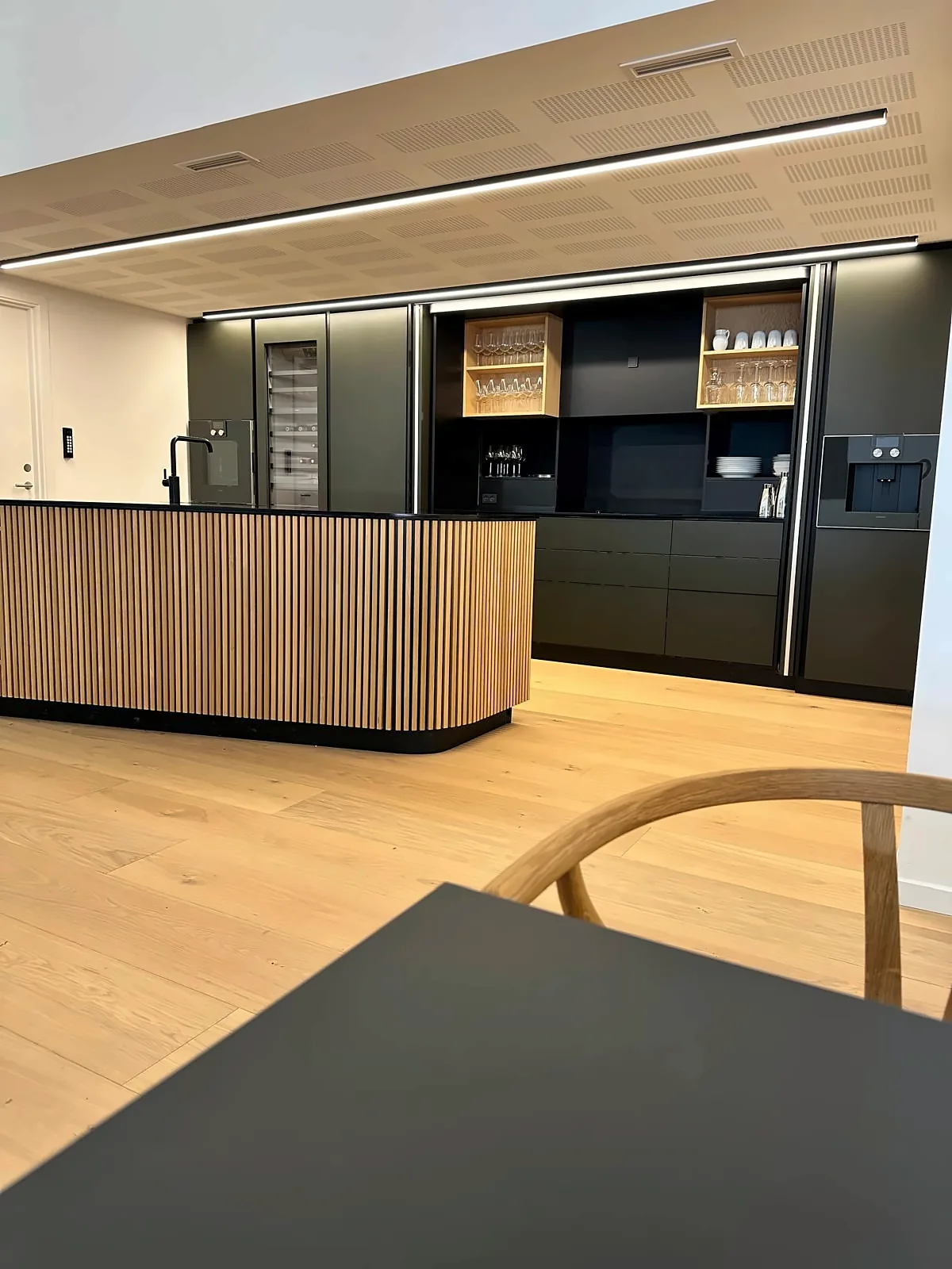 Kaffekjøkken med grønne skap, ribbet eik og akustikktak hos Andersen Biler i Gladsaxe